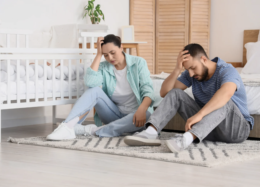 stressed parents sitting next to baby crib