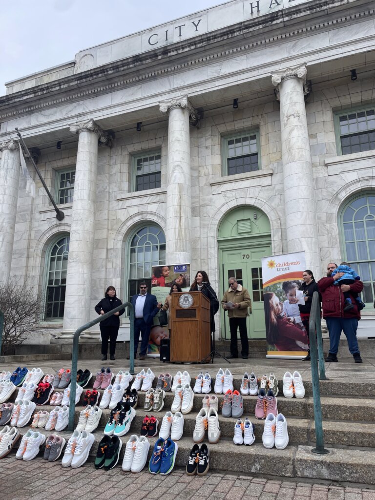 woman speaking at podium with display of children's shoes
