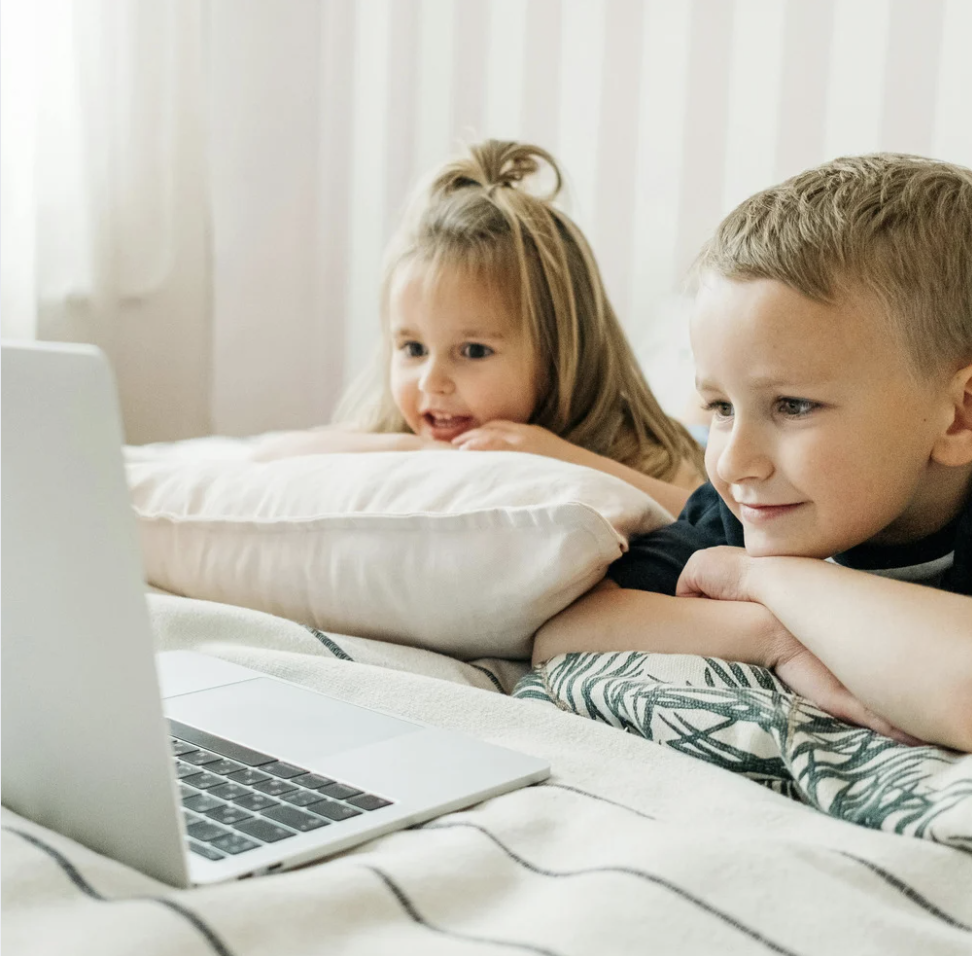 A young boy and girl laying down looking at a computer screen