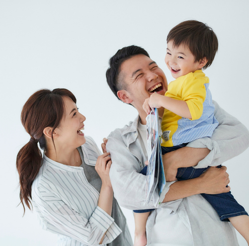 A smiling man holds a laughing young boy in his arms while a woman stands beside them, all sharing a moment of joy against a plain white background.