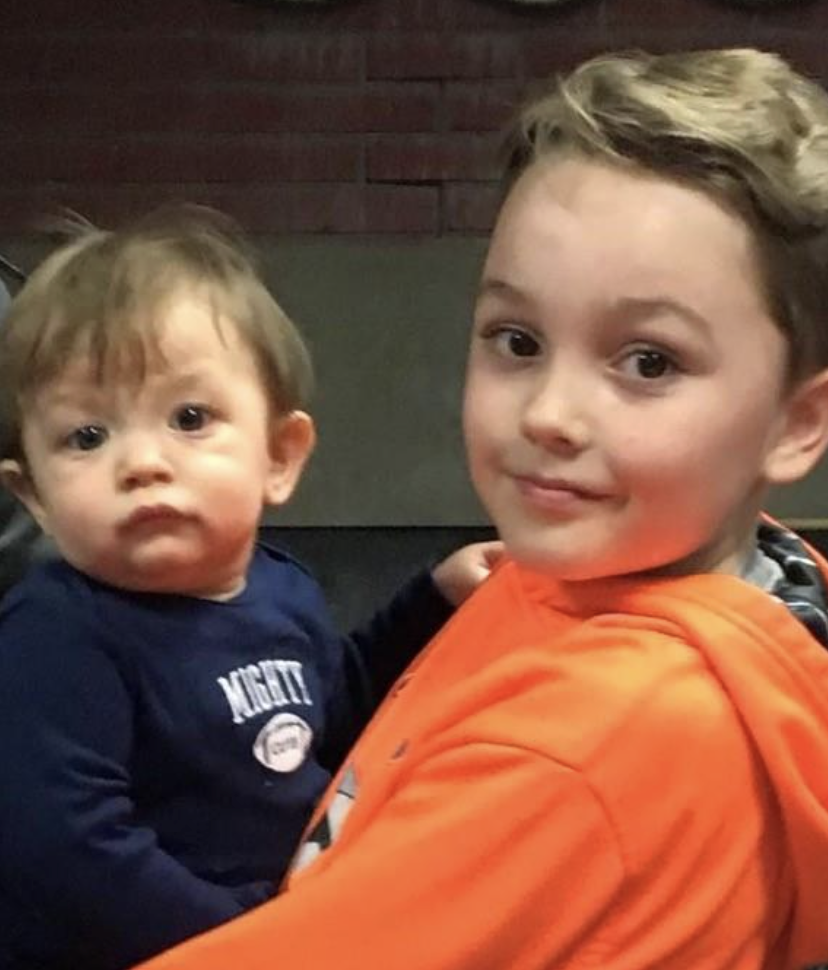 A young boy in an orange hoodie holds a baby wearing a navy blue shirt.