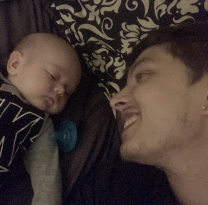 Andrew laying next to his sleeping baby smiling at him