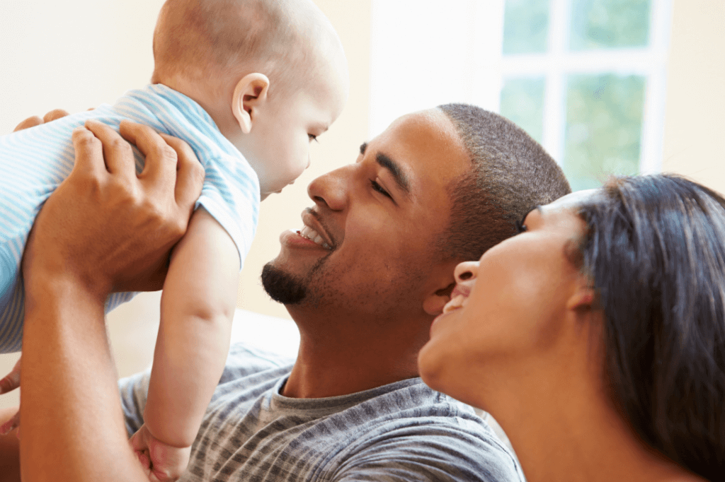 father holding baby up in the air and mother next to them smiling