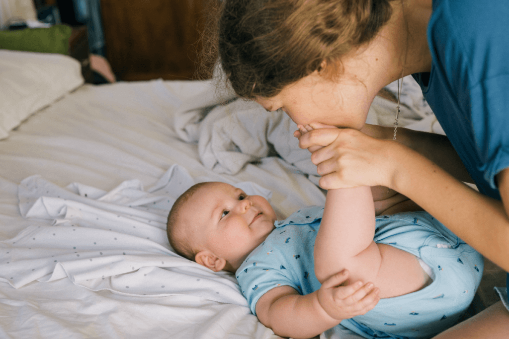 mother kissing baby's feet with baby laying on bed smiling