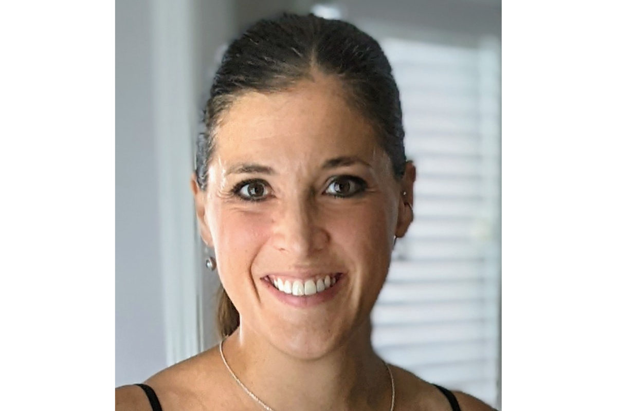 A woman with long brown hair pulled back, wearing a black top, small earrings, and a necklace—Michaela Gagne, CAGS, LMHC—smiling at the camera in a softly lit indoor setting with blurred background.