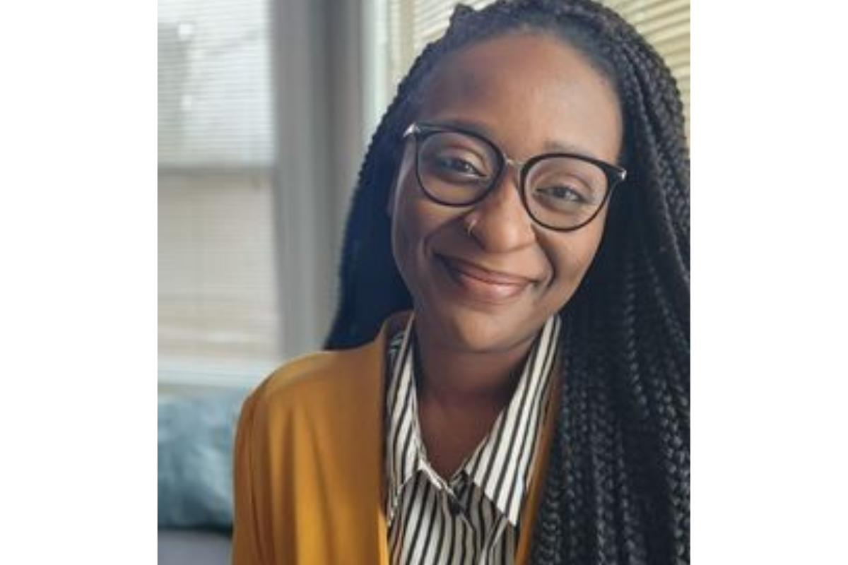 Helen Joseph, LMHC, a smiling woman with long braided hair, glasses, a mustard yellow jacket, and a black-and-white striped shirt, sits indoors with window blinds in the background.