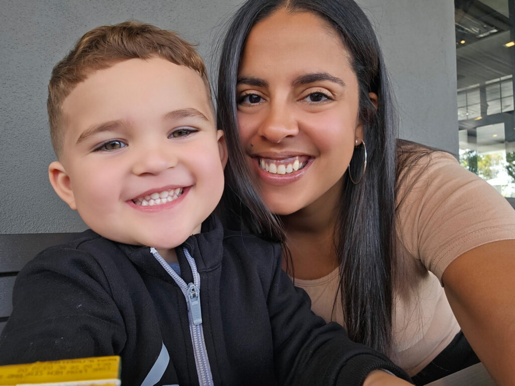 Jessica Ortiz, Healthy Families Program Coordinator with a young boy with short light brown hair in a black jacket. Sitting closely together, they both smile at the camera, celebrating National Home Visiting Week.
