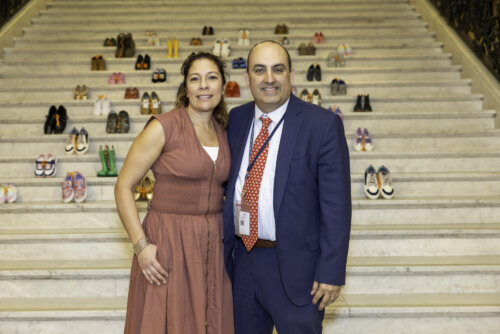 A man and a woman stand on marble stairs lined with dozens of colorful shoes at the Step Up for Kids Boston event.