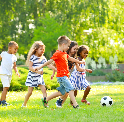 Five children play soccer on a sunny day in a grassy park. Smiling and running with joy.