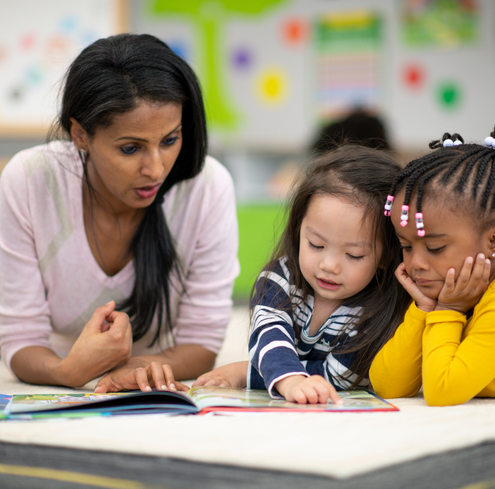 Teacher with two students reading a magazine at a desk.