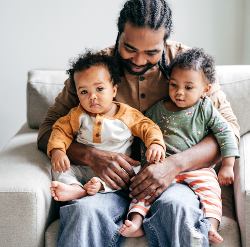 A man sits on a sofa with a baby on each lap.