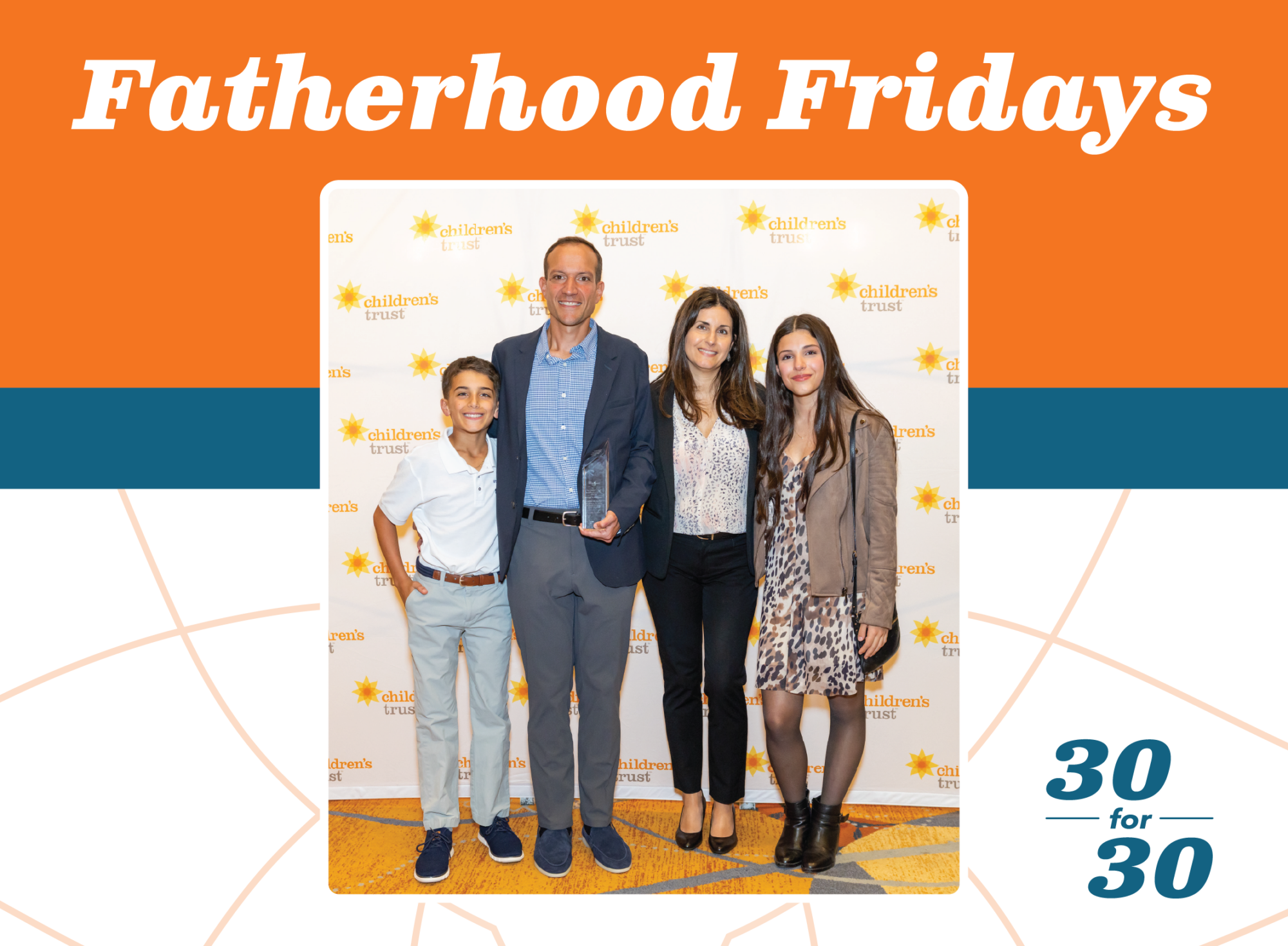 A family of four stands together in front of a Childrens Trust step and repeat banner, with the father celebrating his role in fatherhood as he holds an award.